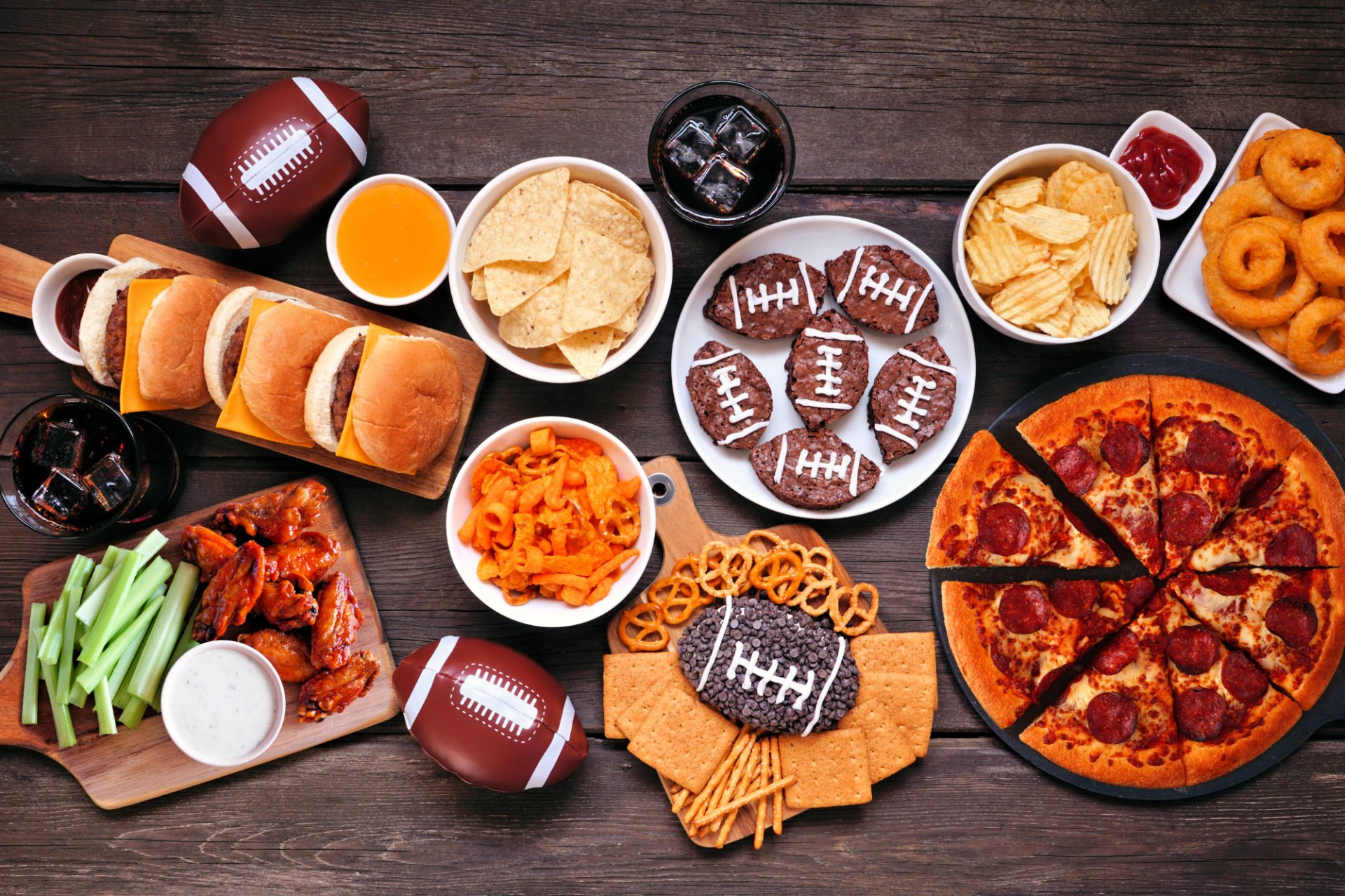 Football-themed tailgate spread with pizza, wings, sliders, chips, and desserts on a wooden table, perfect for pairing with Camino Gummies on game day.